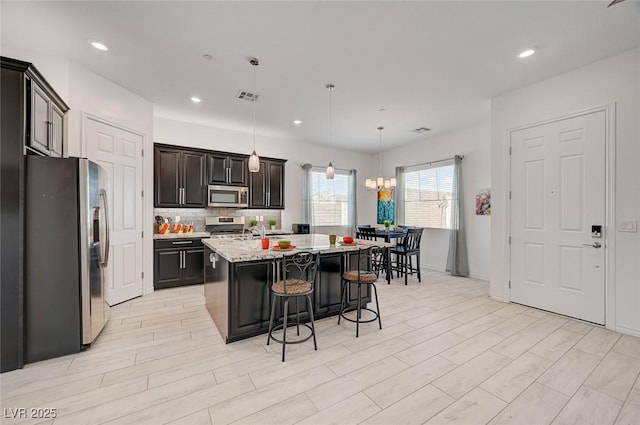 794 Sunny Sagebrush St, Henderson, NV 89011 - kitchen with appliances with stainless steel finishes, a breakfast bar area, a kitchen island with sink, decorative backsplash, and hanging light fixtures