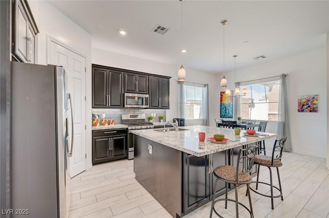 794 Sunny Sagebrush St, Henderson, NV 89011 - kitchen featuring appliances with stainless steel finishes, an island with sink, light stone countertops, tasteful backsplash, and a breakfast bar