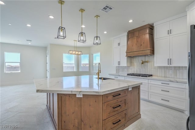 1525 Heights Dr, Logandale, NV 89021 - kitchen featuring premium range hood, stainless steel gas cooktop, light stone counters, decorative backsplash, and a kitchen island with sink