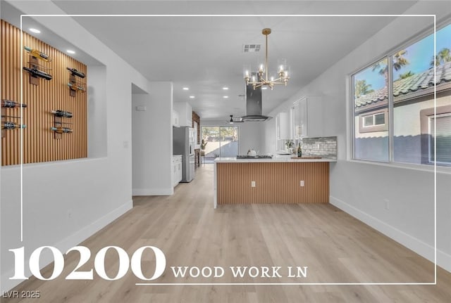 10200 Wood Work Ln, Las Vegas, NV 89135 - kitchen featuring island range hood, appliances with stainless steel finishes, a peninsula, light wood-style floors, and white cabinetry