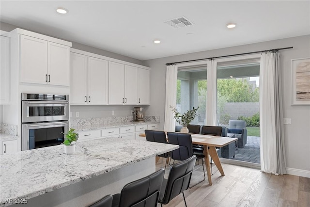12426 Alpenglow Ct, Las Vegas, NV 89138 - kitchen with double oven, a breakfast bar area, white cabinetry, light stone counters, and recessed lighting