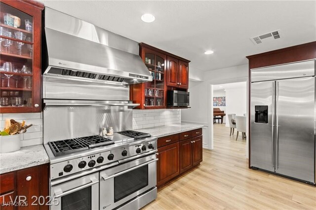 3108 Sonia Dr, Las Vegas, NV 89107 - kitchen with high end appliances, wall chimney exhaust hood, light wood-style floors, backsplash, and light stone countertops