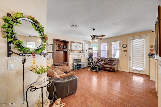 3873 Palm Island Ct, Las Vegas, NV 89147 - living area featuring a tile fireplace, light wood-type flooring, ceiling fan, and a textured ceiling