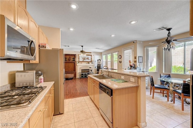 3873 Palm Island Ct, Las Vegas, NV 89147 - kitchen featuring ceiling fan, appliances with stainless steel finishes, light brown cabinets, a tiled fireplace, and recessed lighting