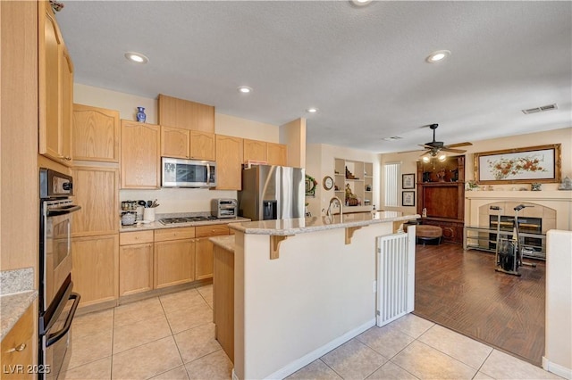 3873 Palm Island Ct, Las Vegas, NV 89147 - kitchen featuring appliances with stainless steel finishes, light brown cabinetry, a breakfast bar, light tile patterned flooring, and a ceiling fan