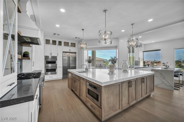 2058 Troon Dr, Henderson, NV 89074 - kitchen with built in appliances, a large island with sink, a chandelier, premium range hood, and light wood-type flooring