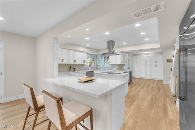2868 Vista Del Sol Ave, Las Vegas, NV 89120 - kitchen with a peninsula, stainless steel dishwasher, island range hood, light wood-style flooring, and white cabinetry