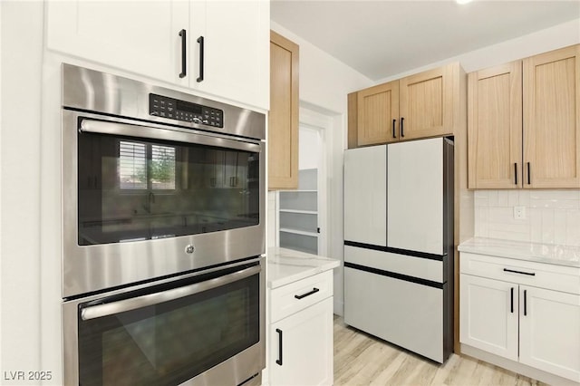 10302 Artful Stone Ave, Las Vegas, NV 89149 - kitchen with freestanding refrigerator, stainless steel double oven, light wood finished floors, tasteful backsplash, and light stone countertops