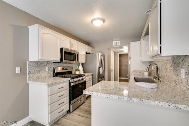 507 Satin Saddle Pl, Henderson, NV 89052 - kitchen with stainless steel appliances, decorative backsplash, white cabinetry, light stone countertops, and light wood finished floors