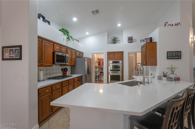 2640 Torch Ave, North Las Vegas, NV 89081 - kitchen featuring stainless steel appliances, a peninsula, a kitchen breakfast bar, brown cabinets, and backsplash