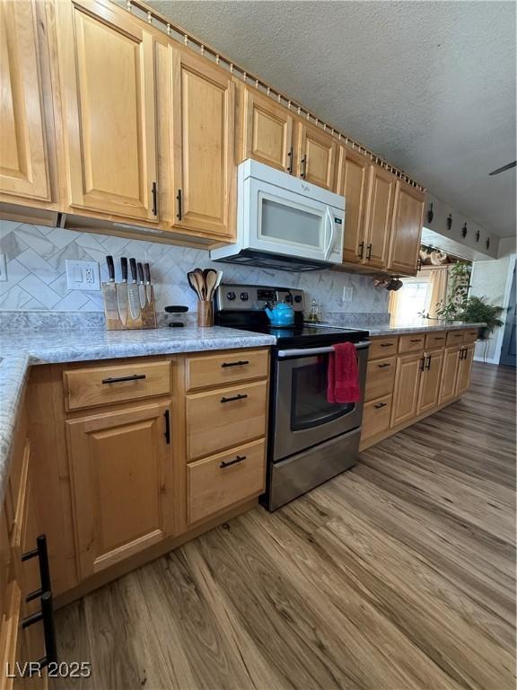 1829 Campton St, Ely, NV 89301 - kitchen with white microwave, electric stove, light wood-style flooring, a textured ceiling, and backsplash