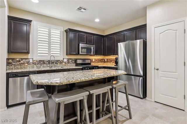7407 Bakewell Ave, Las Vegas, NV 89179 - kitchen with appliances with stainless steel finishes, a breakfast bar, dark brown cabinets, light stone counters, and a center island