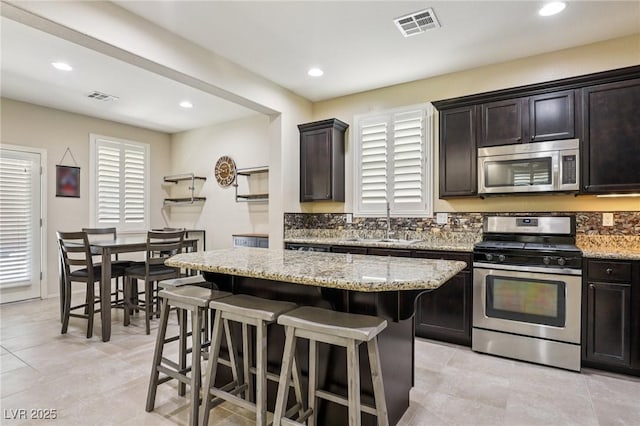 7407 Bakewell Ave, Las Vegas, NV 89179 - kitchen with appliances with stainless steel finishes, a breakfast bar area, light stone counters, a kitchen island, and recessed lighting