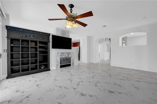 3079 Evening Mist Ave, Henderson, NV 89052 - unfurnished living room featuring light marble finish flooring, arched walkways, ceiling fan, and a high end fireplace