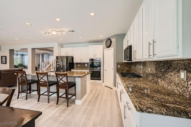 6103 Sundown Crest St, Las Vegas, NV 89113 - kitchen featuring black appliances, a kitchen breakfast bar, white cabinets, light wood-type flooring, and dark stone countertops