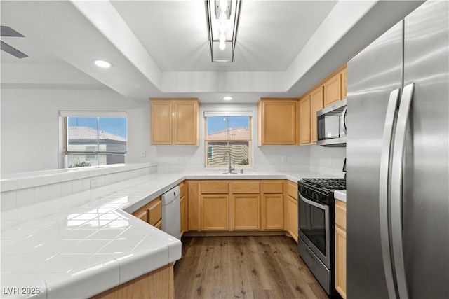 3608 Quetonia St Unit 204, Las Vegas, NV 89108 - kitchen featuring appliances with stainless steel finishes, light brown cabinets, wood finished floors, tile countertops, and a raised ceiling