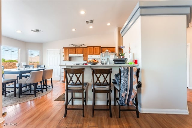 4656 E Desert Inn Rd, Las Vegas, NV 89121 - kitchen with brown cabinetry, light wood-style flooring, refrigerator with ice dispenser, under cabinet range hood, and recessed lighting