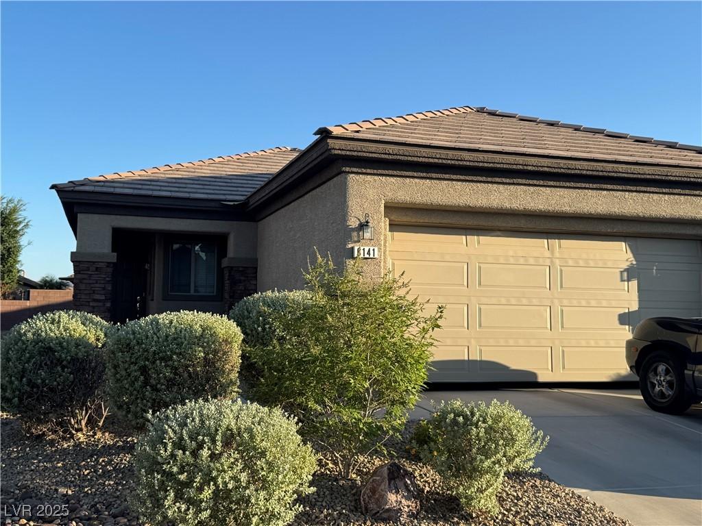 6141 Tokara Ave, Las Vegas, NV 89122 - view of front of home with a tile roof, a garage, stucco siding, concrete driveway, and stone siding