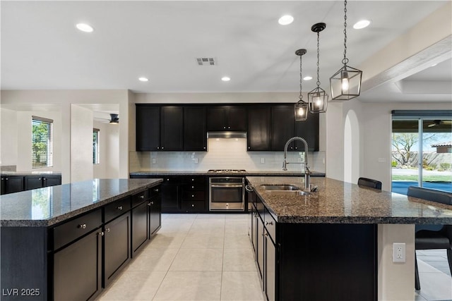 9240 Northfield Park Ct, Las Vegas, NV 89148 - kitchen with a kitchen island with sink, stainless steel appliances, arched walkways, tasteful backsplash, and dark stone counters