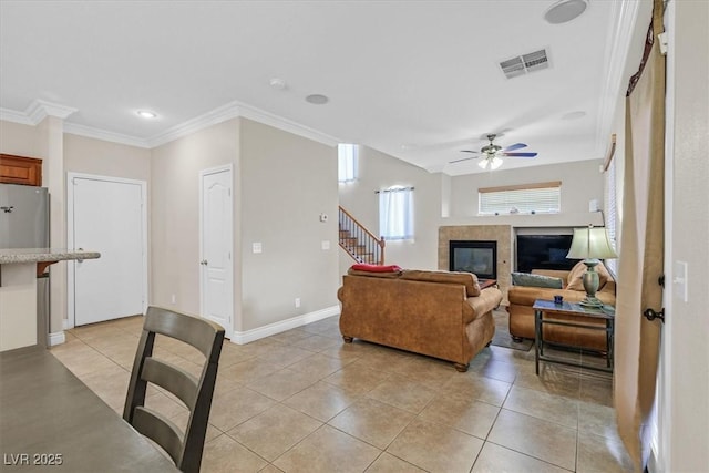 10601 Lessona St, Las Vegas, NV 89141 - living room featuring light tile patterned floors, a tiled fireplace, ceiling fan, stairs, and ornamental molding