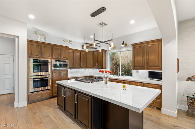11680 Evergreen Creek Ln, Las Vegas, NV 89135 - kitchen featuring appliances with stainless steel finishes, tasteful backsplash, a kitchen island, light wood-type flooring, and a chandelier