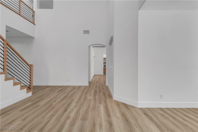1551 Boundary Peak Way, Las Vegas, NV 89135 - unfurnished living room featuring arched walkways, a towering ceiling, light wood-style flooring, and stairway