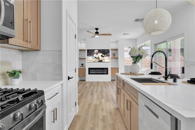 1551 Boundary Peak Way, Las Vegas, NV 89135 - kitchen with appliances with stainless steel finishes, a glass covered fireplace, light wood-style floors, backsplash, and hanging light fixtures