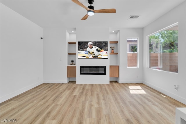 1551 Boundary Peak Way, Las Vegas, NV 89135 - unfurnished living room featuring light wood finished floors, a glass covered fireplace, a ceiling fan, and built in shelves