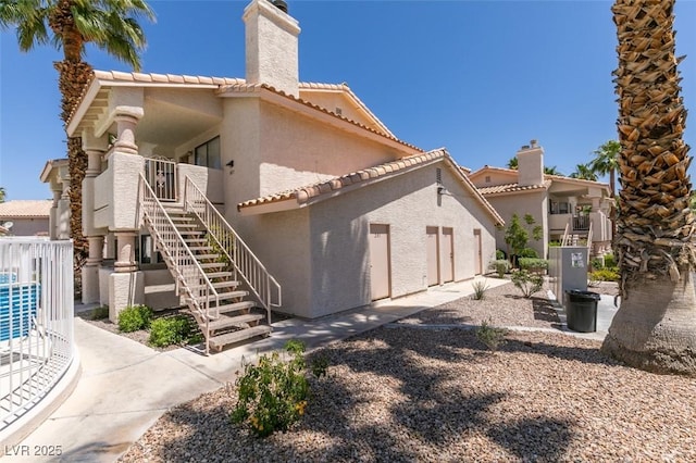 1013 Falconhead Ln Unit 202, Las Vegas, NV 89128 - back of property with stucco siding, stairs, a tiled roof, and a chimney