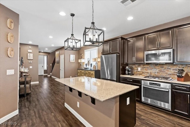 8013 Green River Knob St, Las Vegas, NV 89113 - kitchen featuring appliances with stainless steel finishes, tasteful backsplash, dark brown cabinets, a center island, and a breakfast bar area