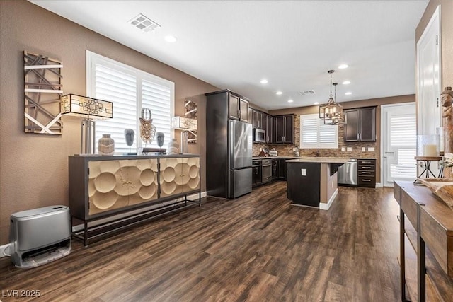 8013 Green River Knob St, Las Vegas, NV 89113 - kitchen with appliances with stainless steel finishes, dark brown cabinetry, dark wood-style flooring, a center island, and backsplash