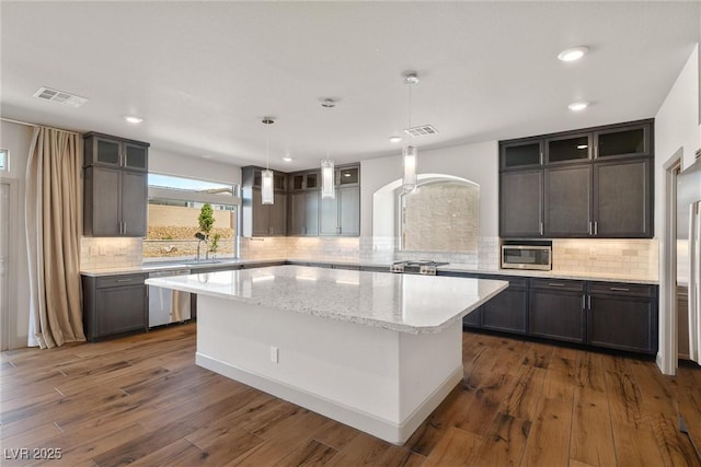 8753 Mann St, Las Vegas, NV 89139 - kitchen with appliances with stainless steel finishes, a kitchen island, glass insert cabinets, dark wood-type flooring, and light stone counters