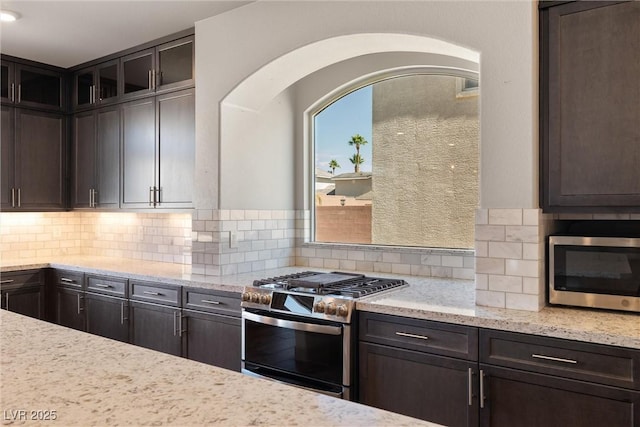 8753 Mann St, Las Vegas, NV 89139 - kitchen with stainless steel appliances, dark brown cabinetry, light stone counters, and backsplash