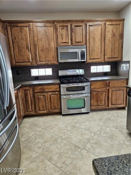 5110 Silenzio St, Las Vegas, NV 89135 - kitchen featuring appliances with stainless steel finishes, dark countertops, decorative backsplash, and brown cabinetry