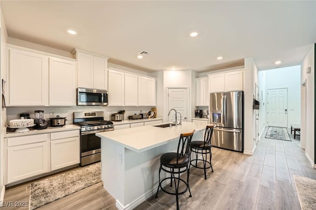 4364 Contour Bend Ave, North Las Vegas, NV 89084 - kitchen with stainless steel appliances, a kitchen bar, light wood finished floors, an island with sink, and white cabinets