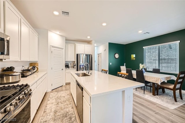 4364 Contour Bend Ave, North Las Vegas, NV 89084 - kitchen with appliances with stainless steel finishes, light wood-style floors, a center island with sink, white cabinets, and recessed lighting
