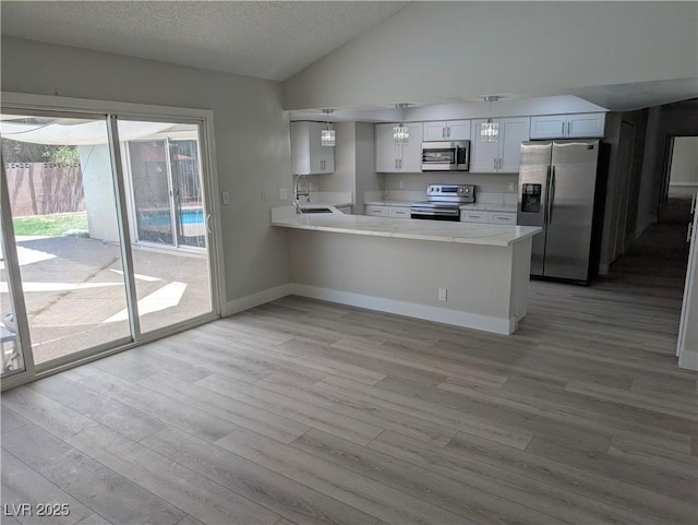 7426 Trudy Ln, Las Vegas, NV 89123 - kitchen featuring appliances with stainless steel finishes, light wood finished floors, a peninsula, light countertops, and lofted ceiling