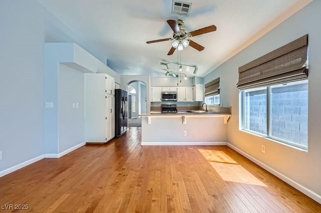 8309 Windrush Ave, Las Vegas, NV 89117 - kitchen featuring black refrigerator, stainless steel microwave, a peninsula, light wood-style flooring, and range
