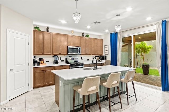 7502 Lush Oasis Ave, Las Vegas, NV 89113 - kitchen featuring stainless steel appliances, brown cabinetry, a center island with sink, light countertops, and light tile patterned flooring