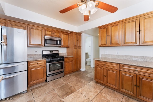 309 Clifton Heights Dr, Las Vegas, NV 89145 - kitchen featuring stainless steel appliances, brown cabinetry, a ceiling fan, light tile patterned floors, and light stone countertops