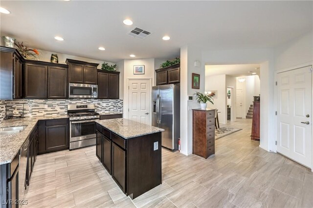 7948 Eastern Elk St, Las Vegas, NV 89149 - kitchen with stainless steel appliances, dark brown cabinetry, light stone counters, backsplash, and a center island