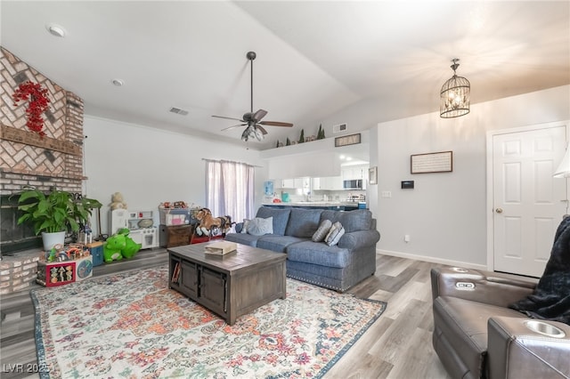 2230 Wagon Ave, Pahrump, NV 89048 - living room featuring vaulted ceiling, light wood-style floors, a brick fireplace, ceiling fan, and a chandelier