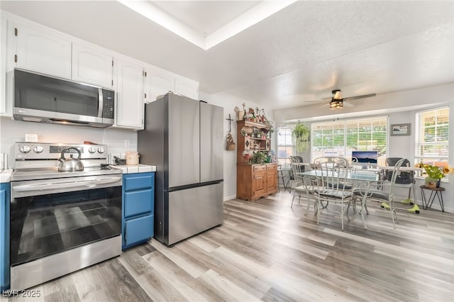2230 Wagon Ave, Pahrump, NV 89048 - kitchen with stainless steel appliances, white cabinets, light wood-type flooring, blue cabinets, and ceiling fan