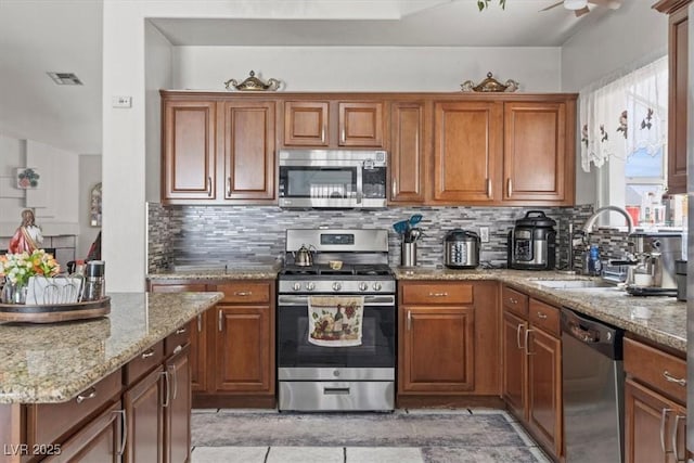 6292 Belgium Dr, Las Vegas, NV 89122 - kitchen with appliances with stainless steel finishes, backsplash, brown cabinetry, light stone counters, and light tile patterned floors