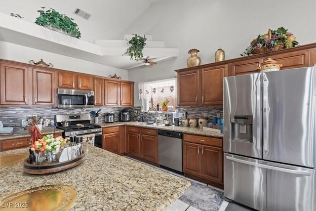 6292 Belgium Dr, Las Vegas, NV 89122 - kitchen with appliances with stainless steel finishes, high vaulted ceiling, decorative backsplash, light stone counters, and light tile patterned floors
