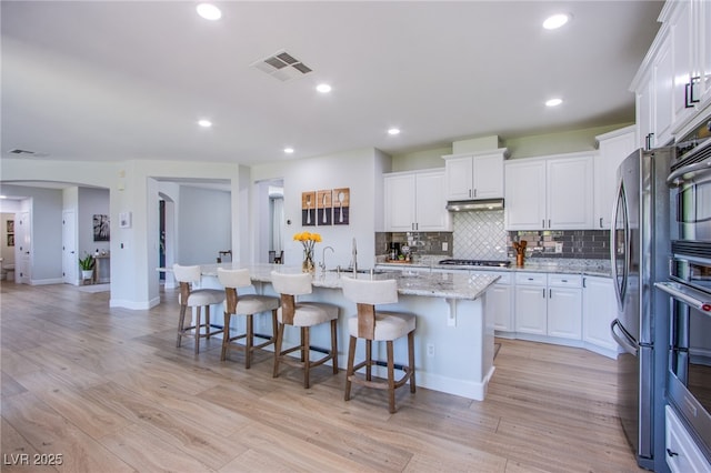 7445 Mezzanine View Ave, Las Vegas, NV 89178 - kitchen with white cabinets, arched walkways, tasteful backsplash, a center island with sink, and light wood-style floors