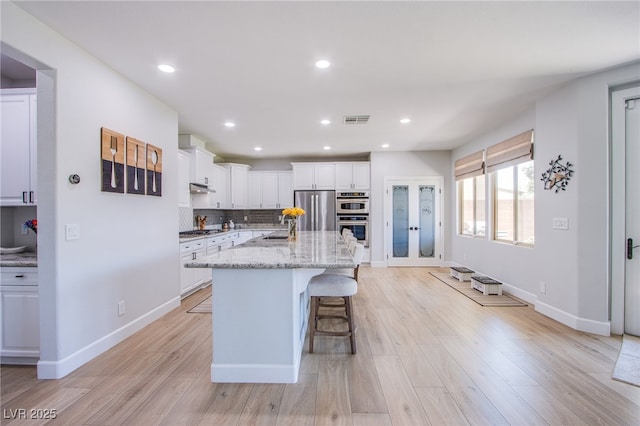7445 Mezzanine View Ave, Las Vegas, NV 89178 - kitchen with stainless steel appliances, white cabinets, a kitchen bar, backsplash, and light wood-style floors