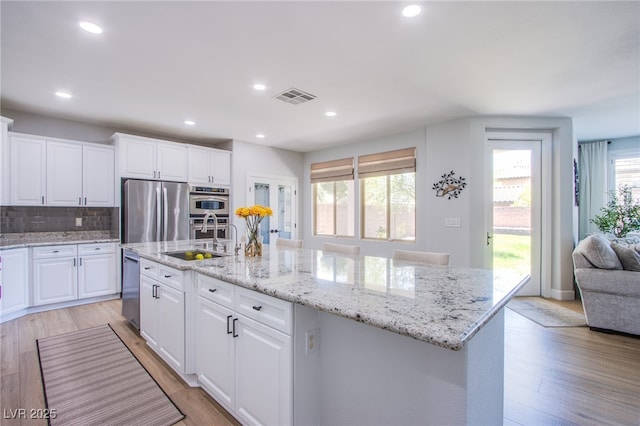 7445 Mezzanine View Ave, Las Vegas, NV 89178 - kitchen featuring appliances with stainless steel finishes, a center island with sink, tasteful backsplash, white cabinetry, and light wood finished floors