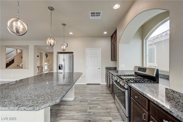 8565 Silver Coast St, Las Vegas, NV 89139 - kitchen featuring stainless steel appliances, dark brown cabinetry, dark stone countertops, light wood finished floors, and recessed lighting