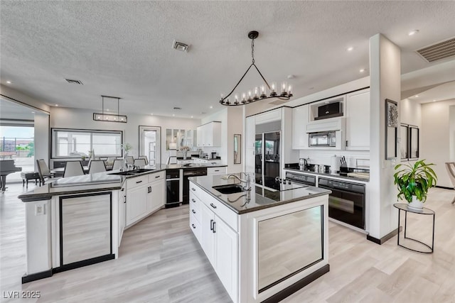 5438 Sierra Brook Ct, Las Vegas, NV 89149 - kitchen featuring black appliances, a kitchen island with sink, a textured ceiling, light wood finished floors, and white cabinets
